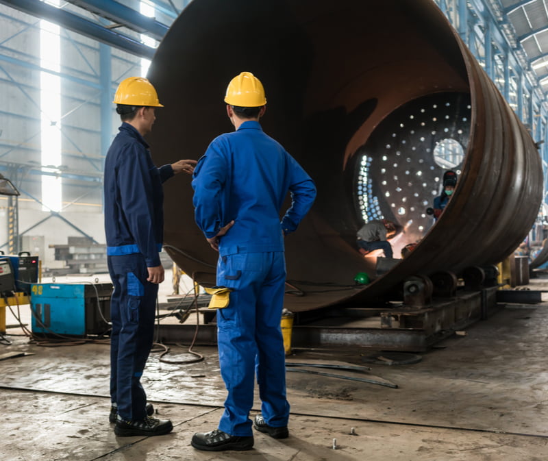 Two experienced workers supervising the manufacture of a metallic cylinder