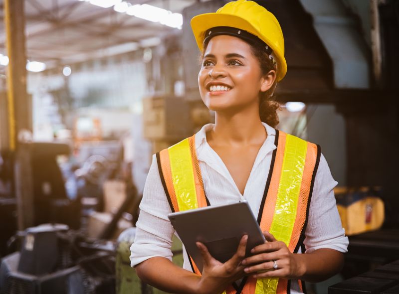 Industry maintenance engineer woman dark skin wearing uniform and safety helmet under inspection and checking production process on factory station by tablet.