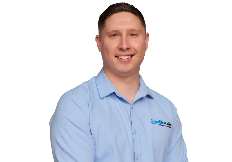 Smiling man in a light blue button-down shirt with a Pilotair logo on the chest, portrait-style head-and-shoulders photo.