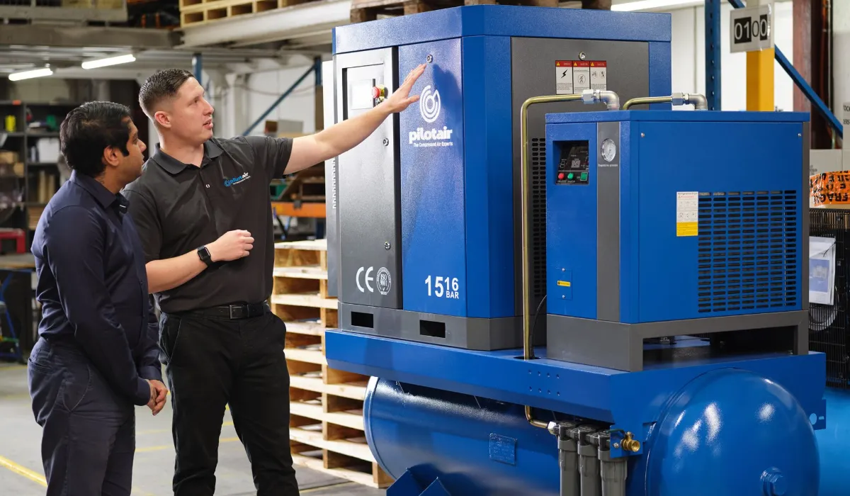 Two workers inspecting an industrial air compressor in a warehouse.