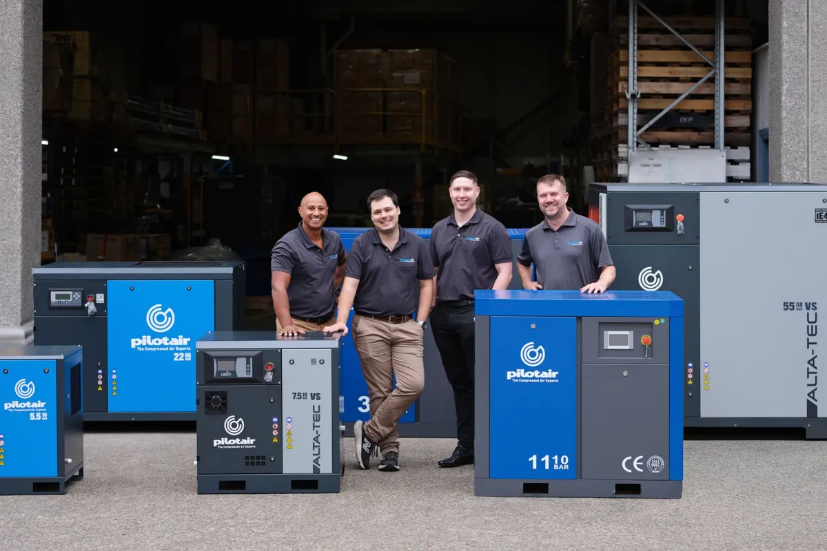 Team of workers standing with industrial air compressors in a warehouse.