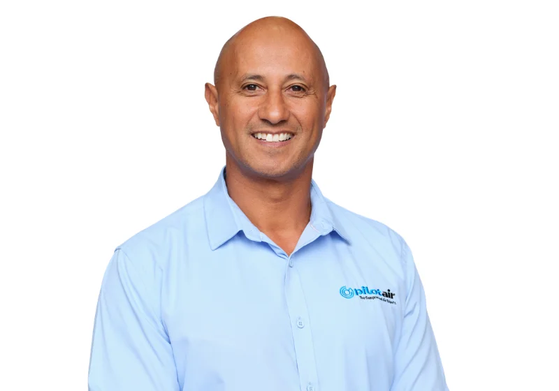 A smiling man in a light blue collared shirt against a plain background.