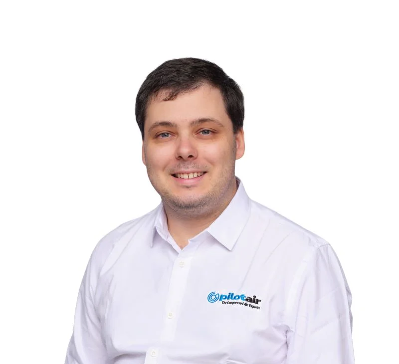 Smiling man in a white button-down shirt with a Pilotair logo on the chest, posing against a white background.