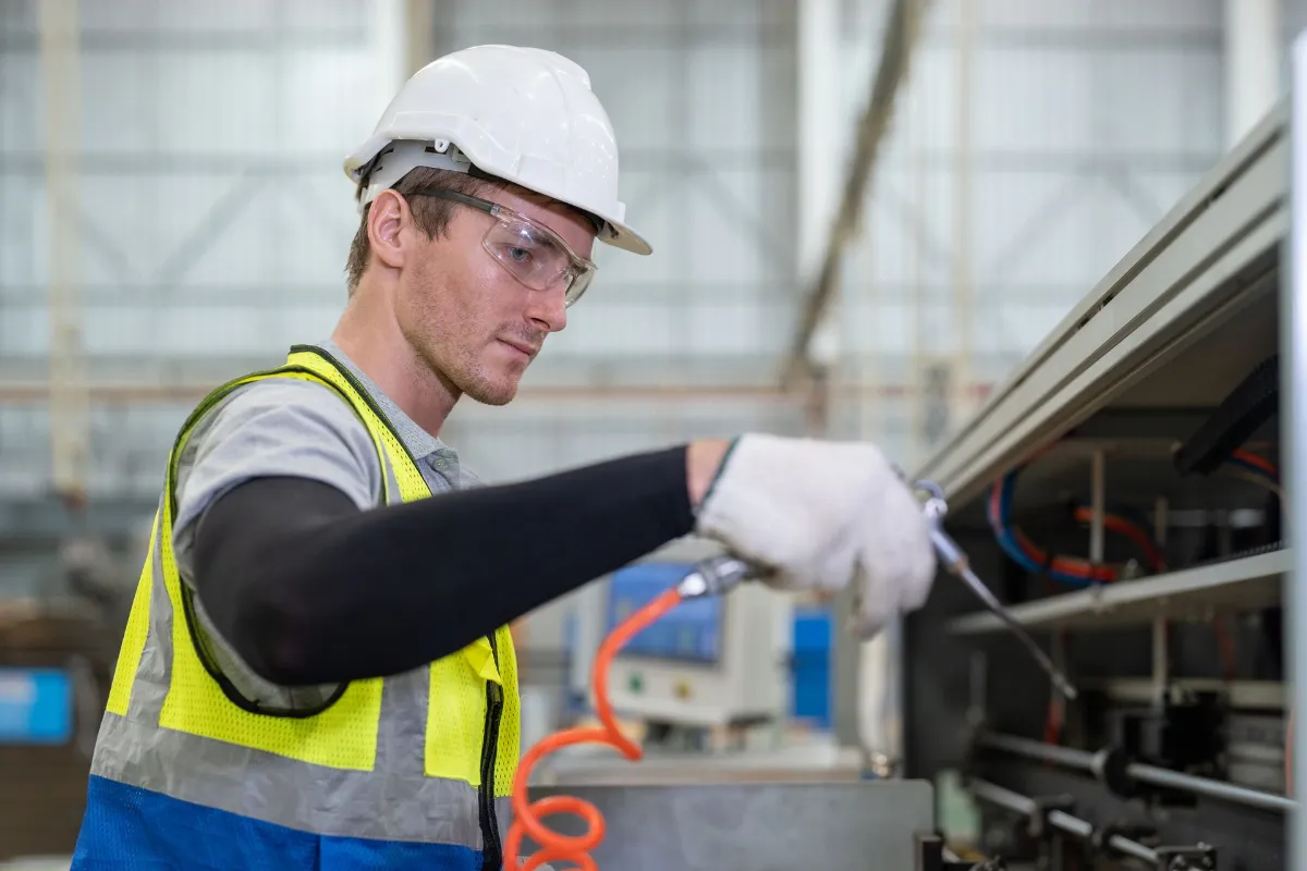 Technician using a tool to service industrial equipment in a factory.